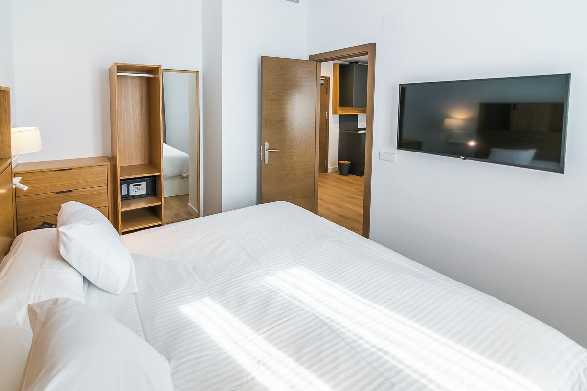 Une chambre d’hôtel comprenant un lit, une armoire, un miroir, une télévision et un bureau avec une lampe.