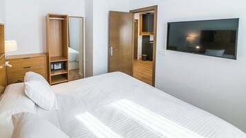 Une chambre d’hôtel comprenant un lit, une armoire, un miroir, une télévision et un bureau avec une lampe.