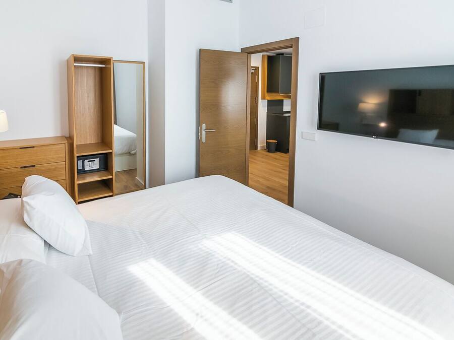 Habitación de hotel con cama, armario, espejo, televisor y escritorio con lámpara.