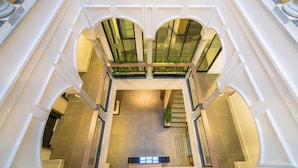 A spacious atrium with a central open area, flanked by white columns and arches, and a lower level with a staircase.