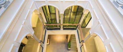 Un vaste atrium doté d’un espace central ouvert, bordé de colonnes et d’arcades blanches, et d’un niveau inférieur accessible par un escalier.