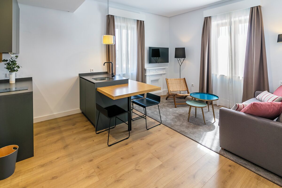 Une chambre d’hôtel moderne avec une table à manger en bois, un canapé, une télévision et une petite table avec des chaises.