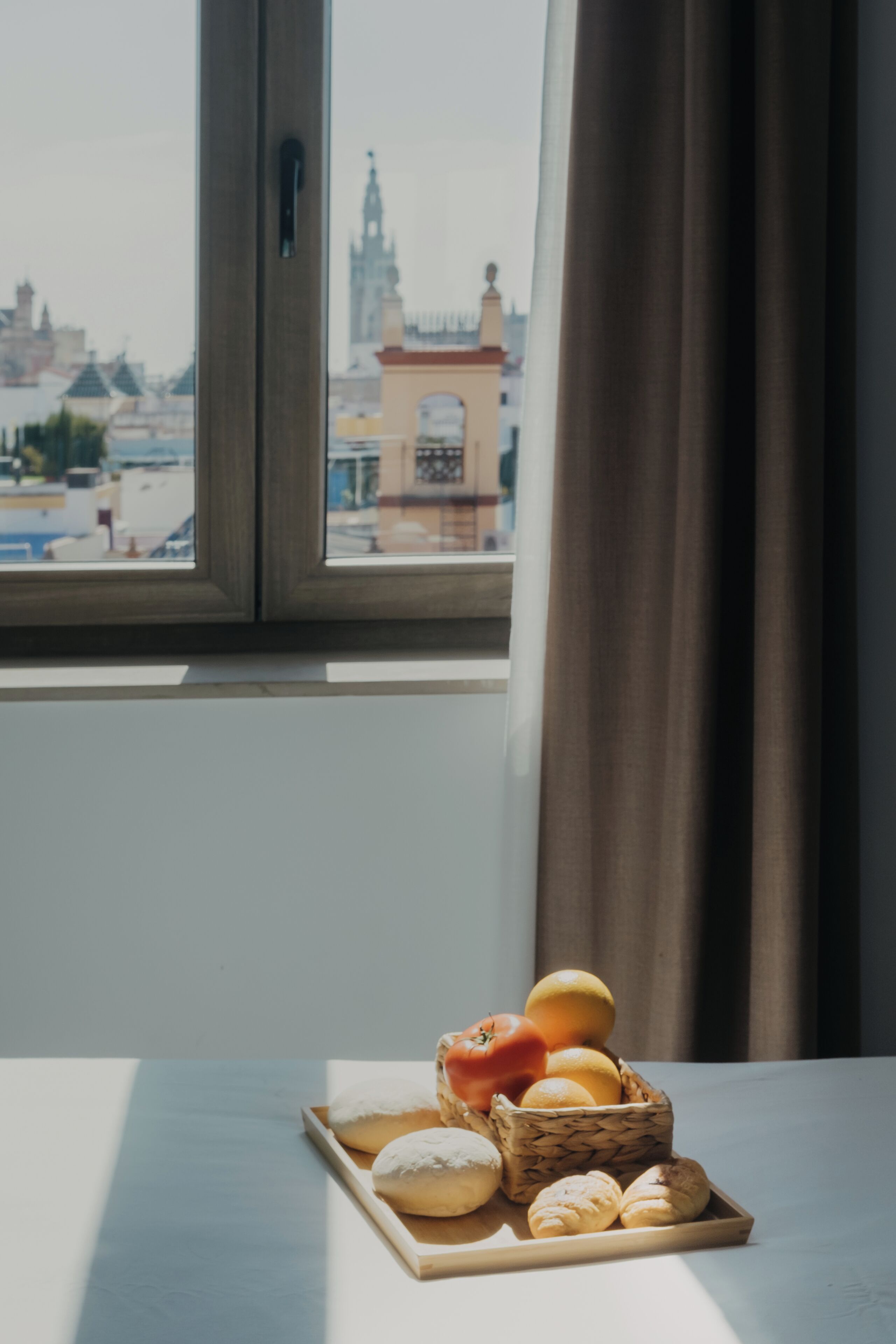 A table with pastries and fruits by a window overlooking a cityscape.