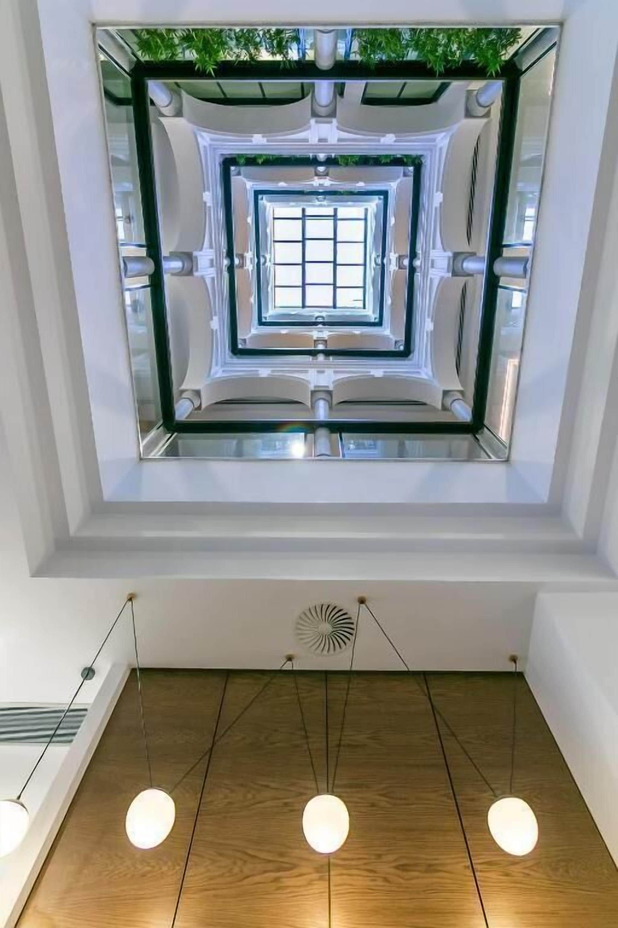 Un interior moderno con un ascensor de vidrio central, suelo de madera e iluminación colgante.