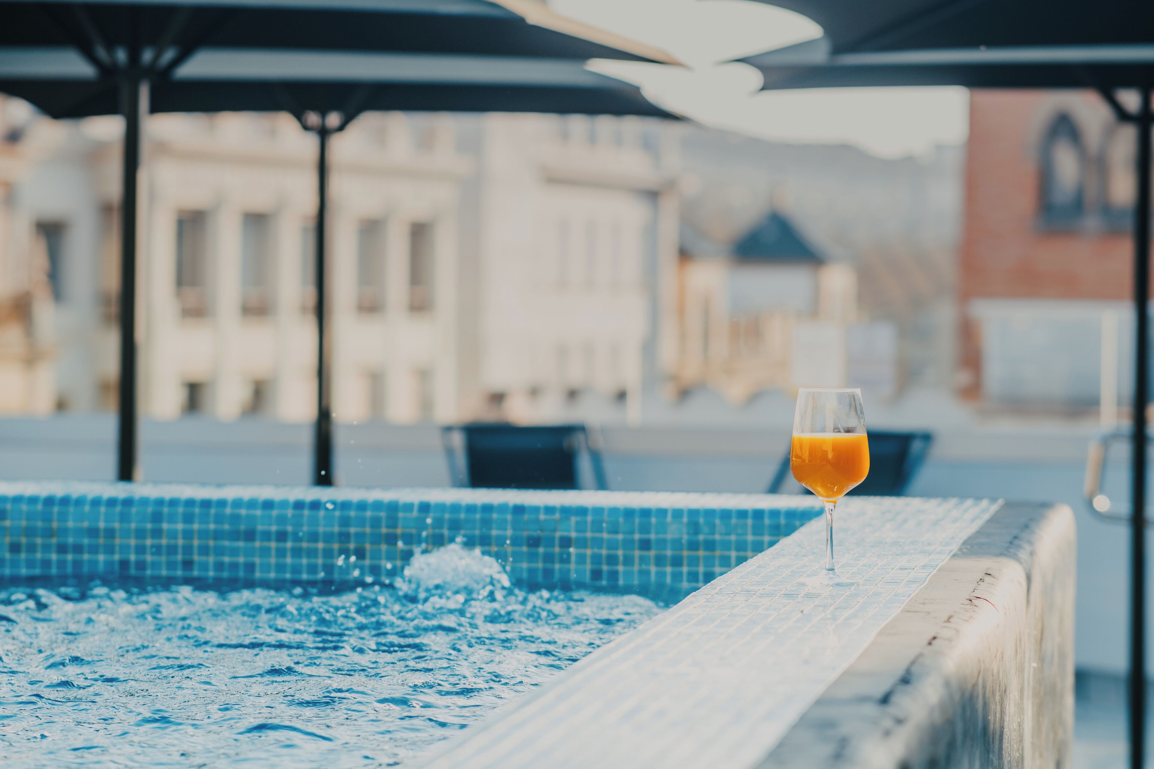 A pool area with a glass of orange juice on the edge, surrounded by a tiled deck and outdoor seating.