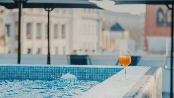 A pool area with a glass of orange juice on the edge, surrounded by a tiled deck and outdoor seating.
