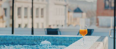A pool area with a glass of orange juice on the edge, surrounded by a tiled deck and outdoor seating.