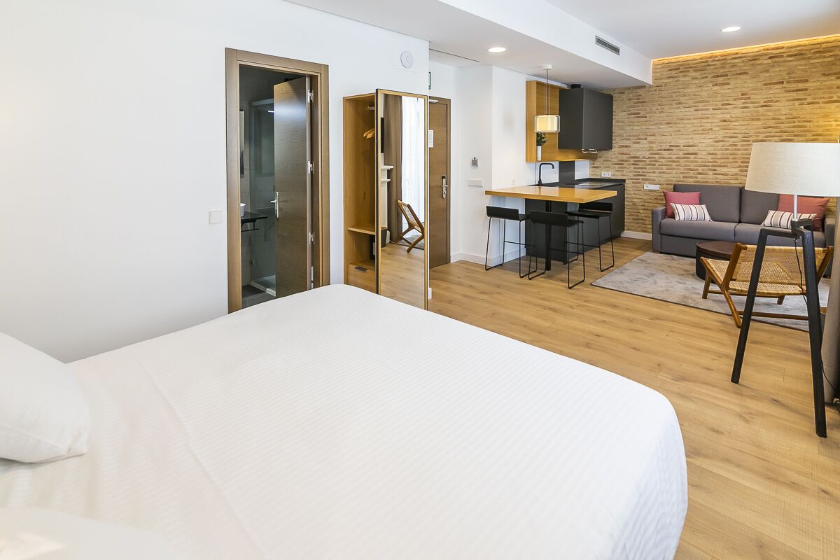 Una habitación de hotel moderna con una cama grande, kitchenette, un sofá y un comedor.