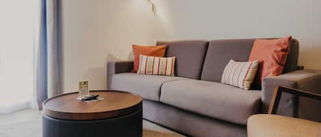 A modern living room with a grey sofa, two striped pillows, a round wooden coffee table, and a wall-mounted lamp.
