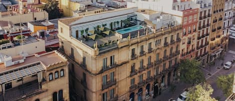 A multi-story building with a rooftop terrace featuring outdoor seating and a swimming pool.