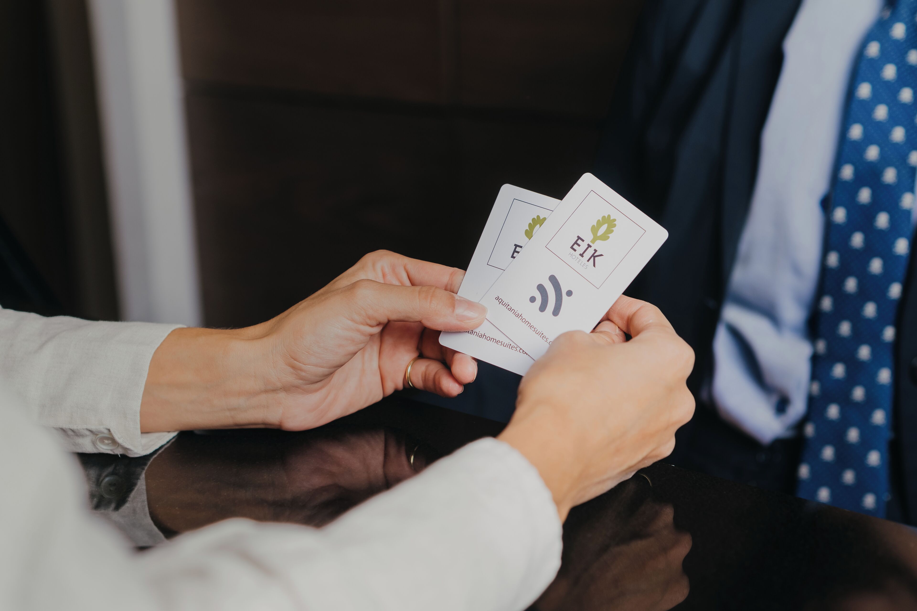 A person holding two business cards with the text "EIK" and "anahomesuites.com".