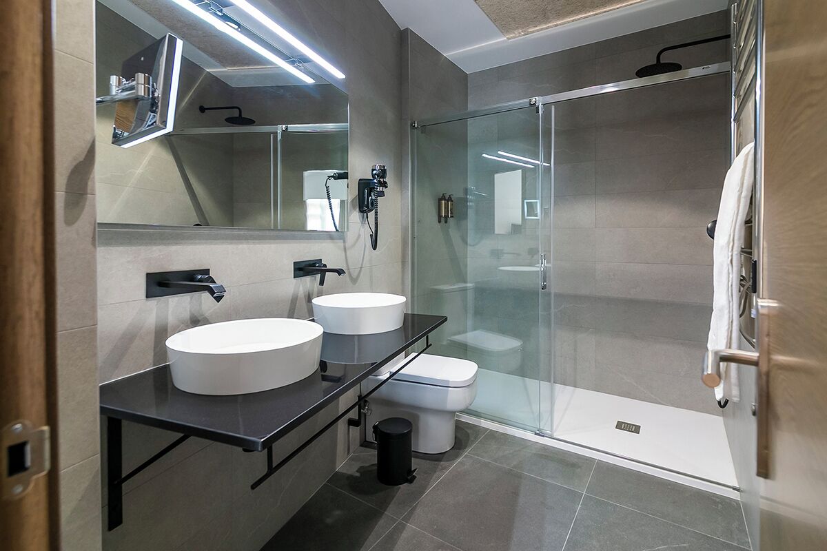 Un baño moderno con dos lavamanos, inodoro y ducha con mampara de vidrio.