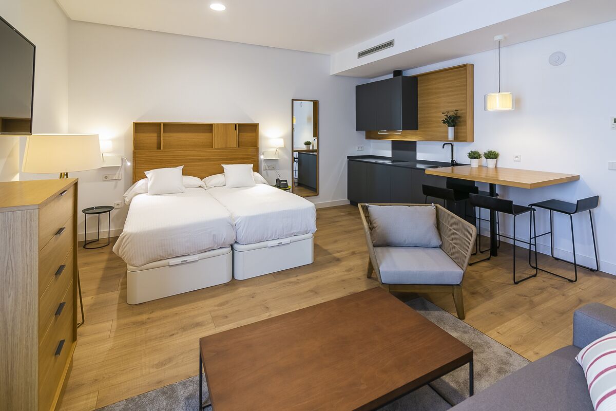 Een moderne hotelkamer met een tweepersoonsbed, een slaapbank, een kleintje tafeltje, een kitchenette en een televisie.