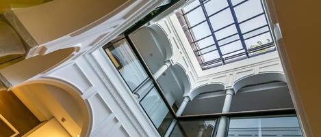 Un atrio espacioso con techos altos y una cubierta de vidrio, adornado con detalles arquitectónicos blancos.