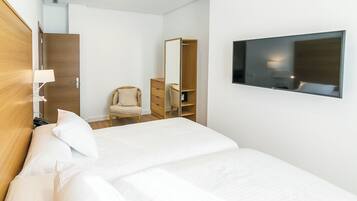 Quarto de hotel com uma cama, uma cadeira, um guarda-roupa e uma televisão na parede.