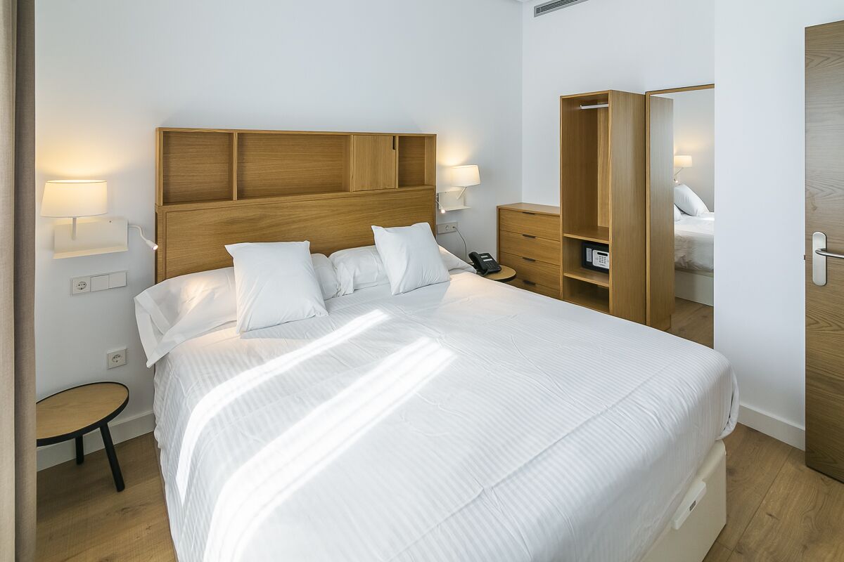 A neatly made bed with a wooden headboard, bedside lamps, a small table, and a wardrobe with a mirror.
