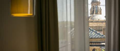 A view through a window with a lamp and curtains, revealing a building with a dome and tiled roof.