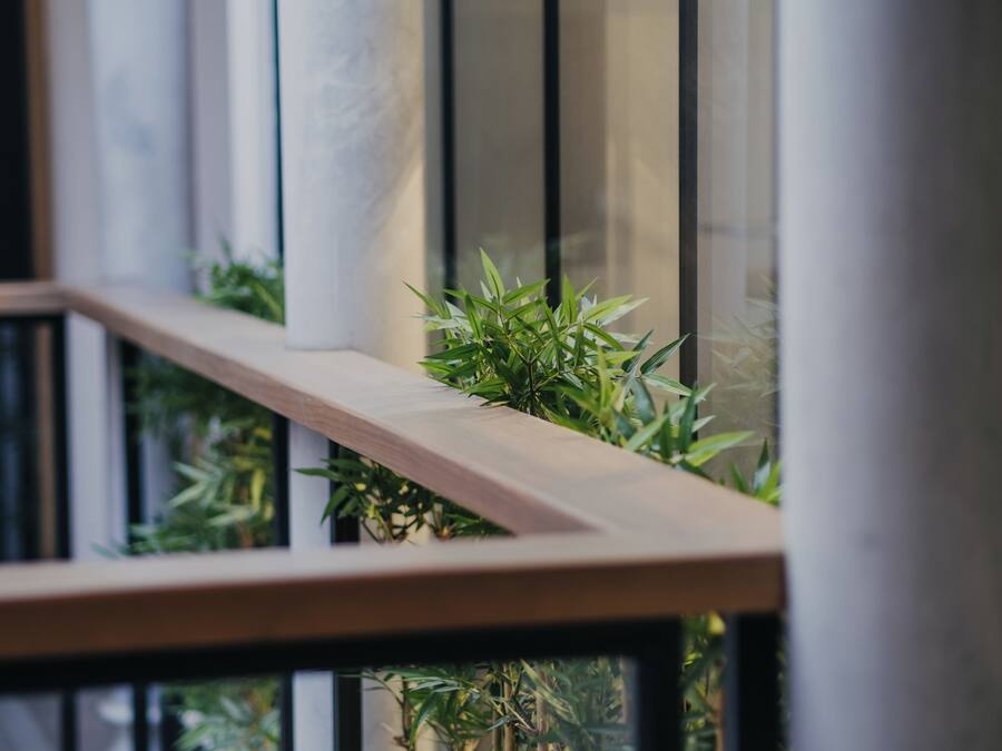 A modern interior with a wooden railing, a potted plant, and a view through a window with vertical blinds.