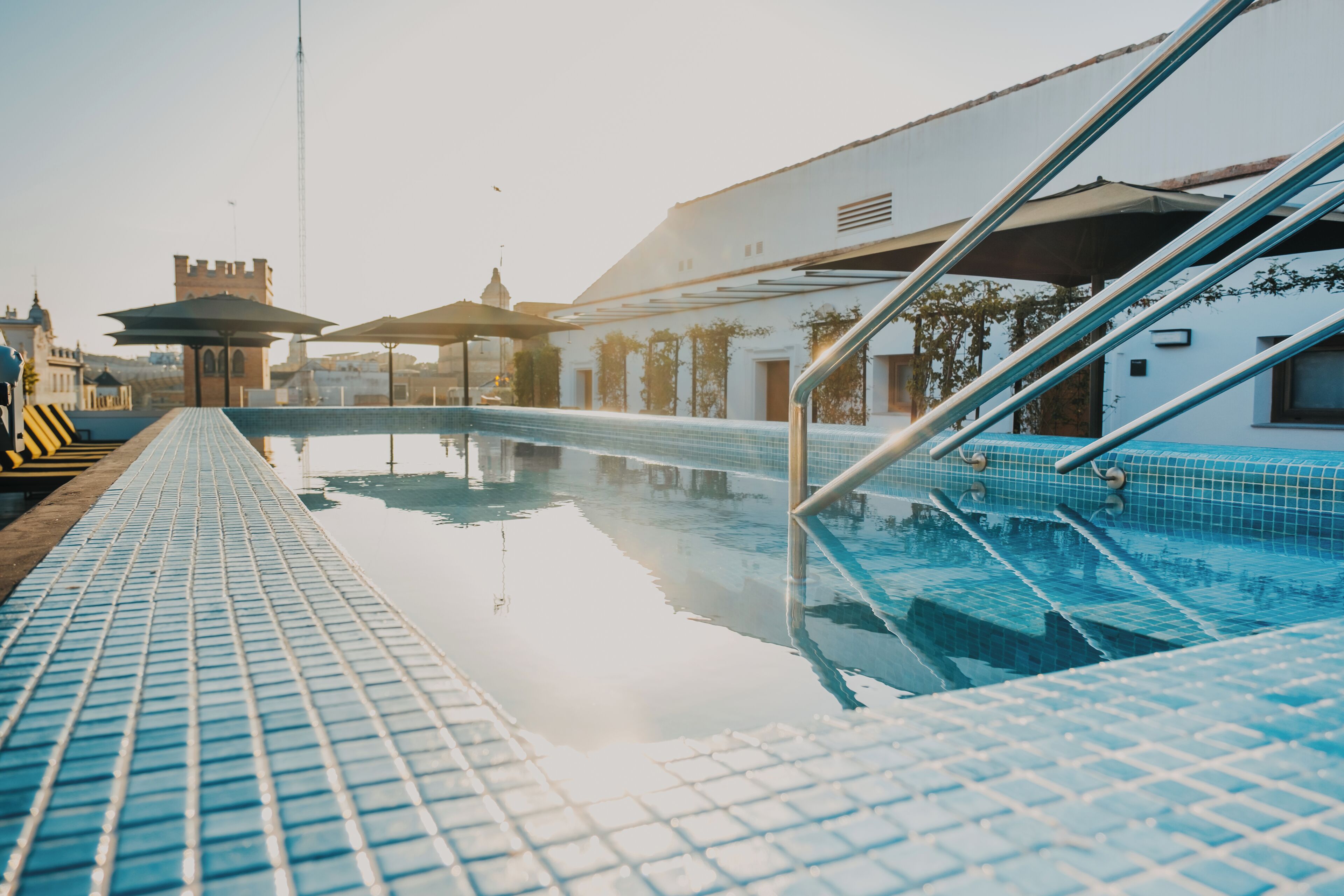 A swimming pool with tiled steps leading into it, surrounded by buildings and a clear sky.