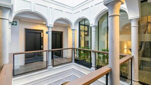 A spacious atrium with white columns, a glass railing, and a view of indoor plants.