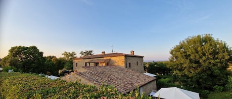 A stone building with a tiled roof, surrounded by greenery and trees.