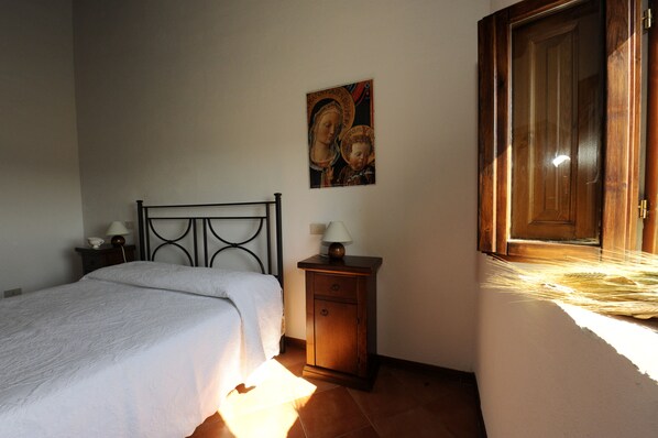 Une chambre à coucher comprenant un lit, une table de chevet, une petite armoire, un tableau accroché au mur et une fenêtre avec un cadre en bois.