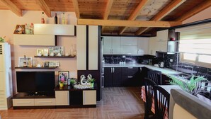 A modern kitchen with wooden beams, a built-in TV, and a dining area with a table and chairs.