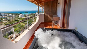 A balcony with a hot tub, a chair, and a view of the sea and buildings.