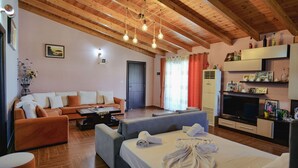 A modern hotel room with a wooden ceiling, a sofa set, a bed, a TV, and a minibar.
