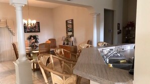 A dining area with wicker chairs, a glass-top table, and a kitchen area with a sink and cabinets.