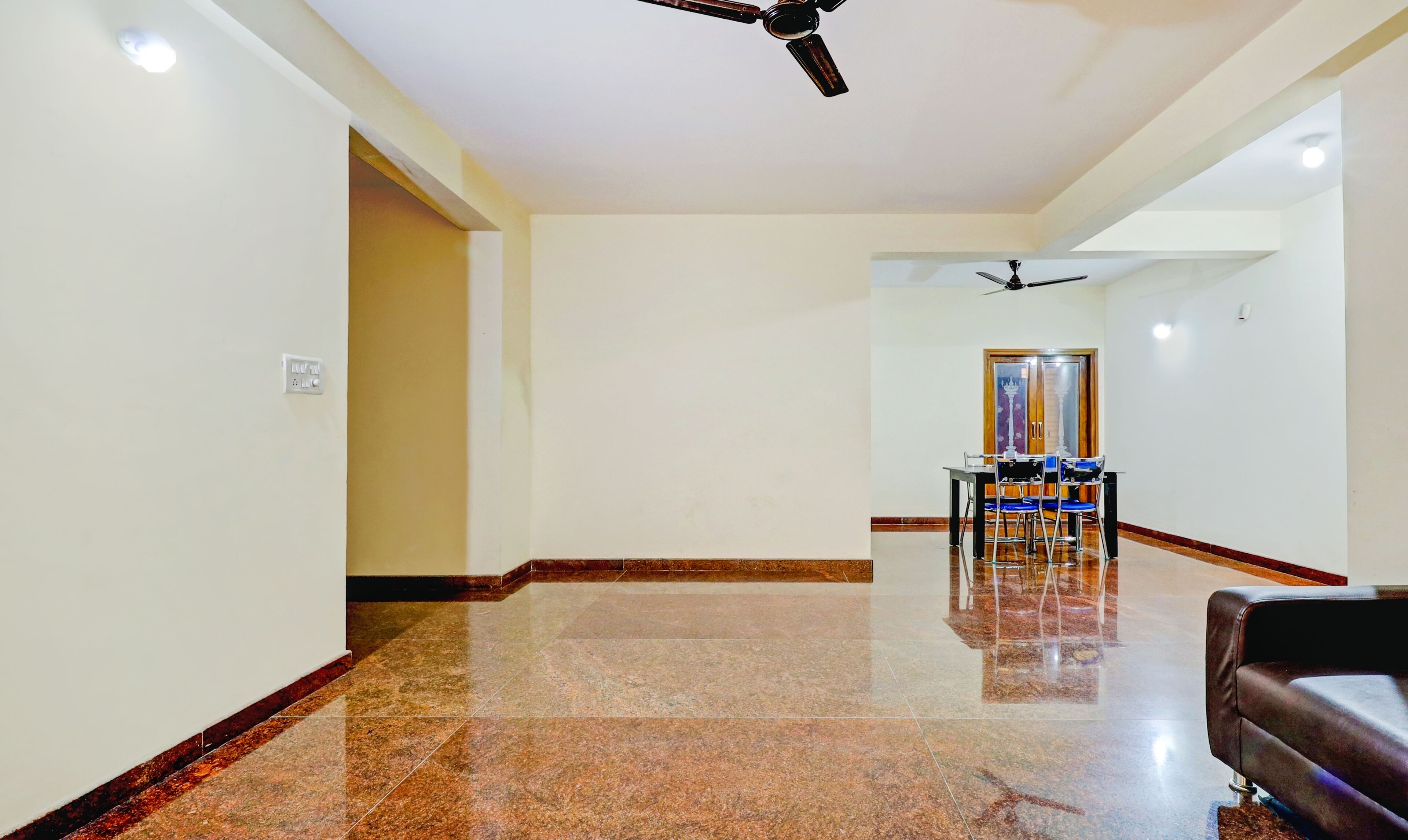A spacious corridor with a polished floor, a dining area with chairs and a table, and a ceiling fan.