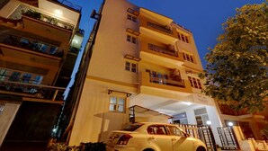 Un hotel de varios pisos con balcones, un coche estacionado en la entrada y un cartel que indica 'The Banagaras Suites'.