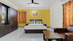Habitación de hotel con cama, escritorio, silla, armario, ventilador de techo y cortinas.