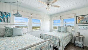 Une chambre avec deux lits, un ventilateur de plafond et vue sur la plage.