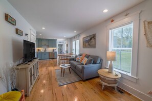A spacious living area with a sofa, a TV, and a dining table. - Second Wind Townhouse, Walk to Beach & Downtown (Cape Charles)