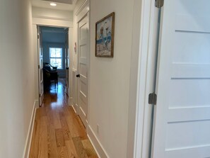 A hallway with wooden flooring, white walls, and a door with a picture frame.