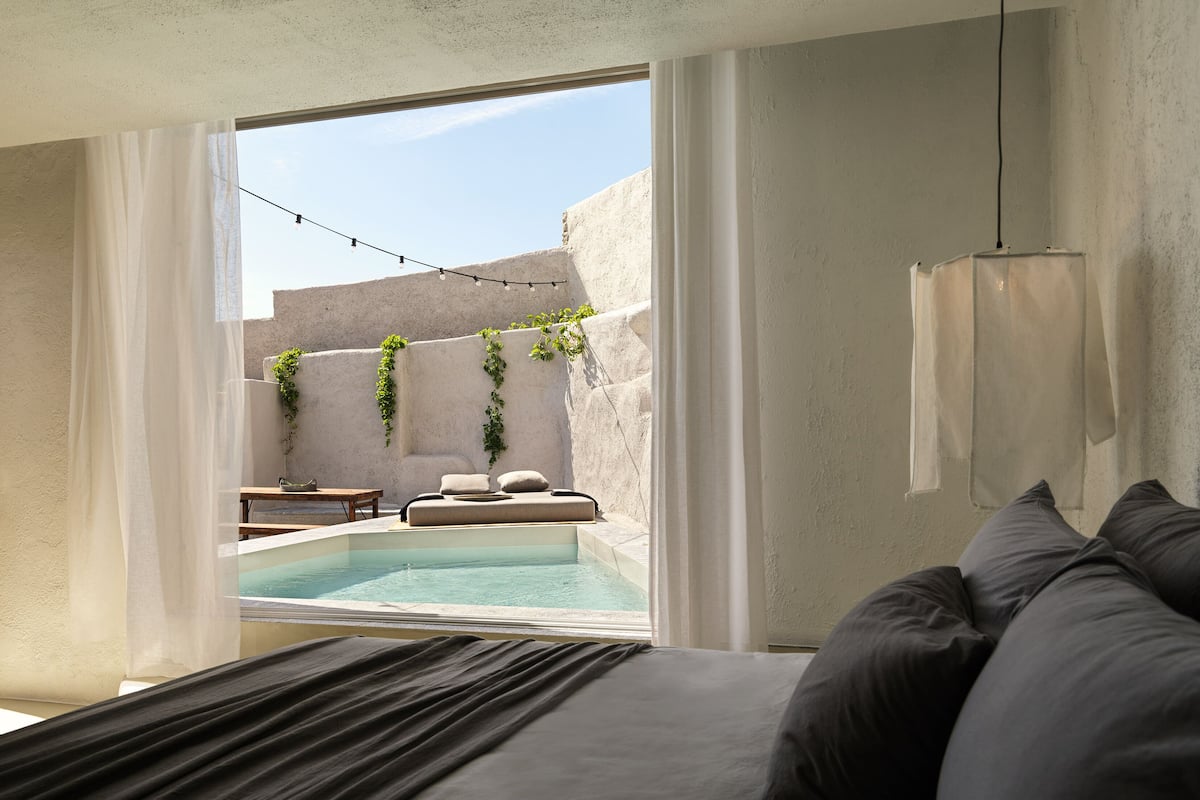 A modern bedroom with a large bed, a view of an outdoor swimming pool, and a hanging light fixture.