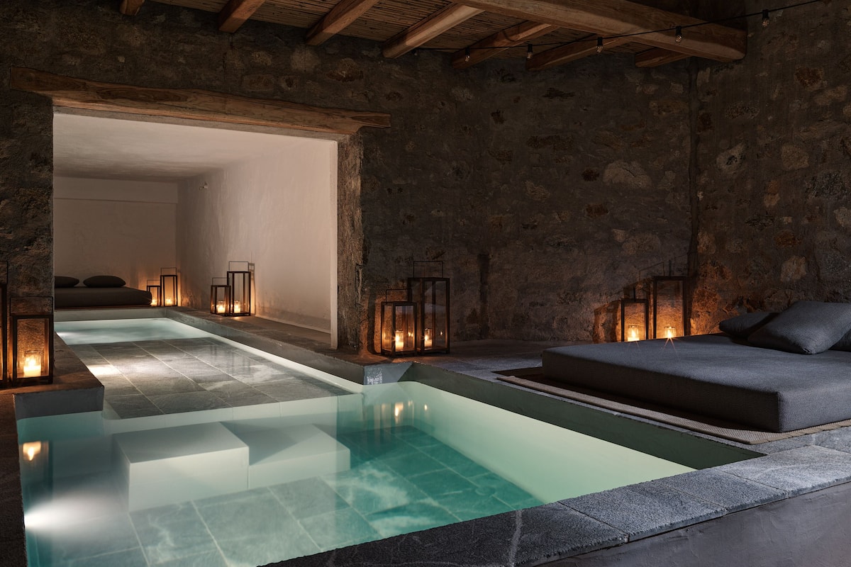 A spa area with a pool, stone walls, wooden beams, and seating.