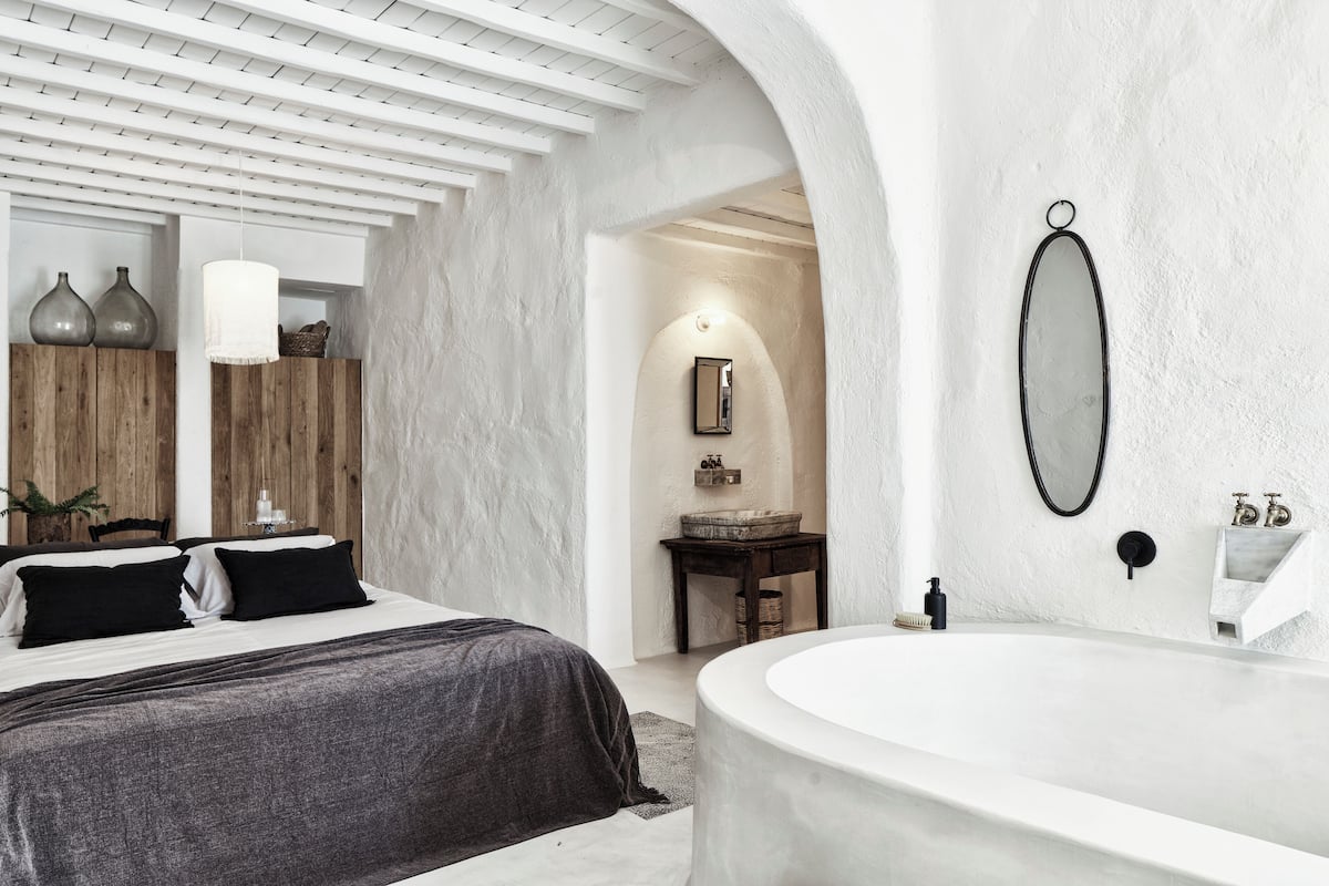 A modern bedroom with a large bed, a white bathtub, and a wooden vanity.