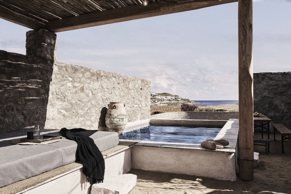 A stone-walled outdoor area with a pool, wooden benches, and a view of the sea.