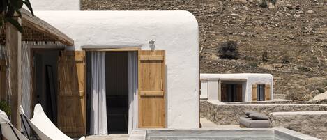 A white-washed villa with a pool, wooden doors, and a view of a rocky hillside.