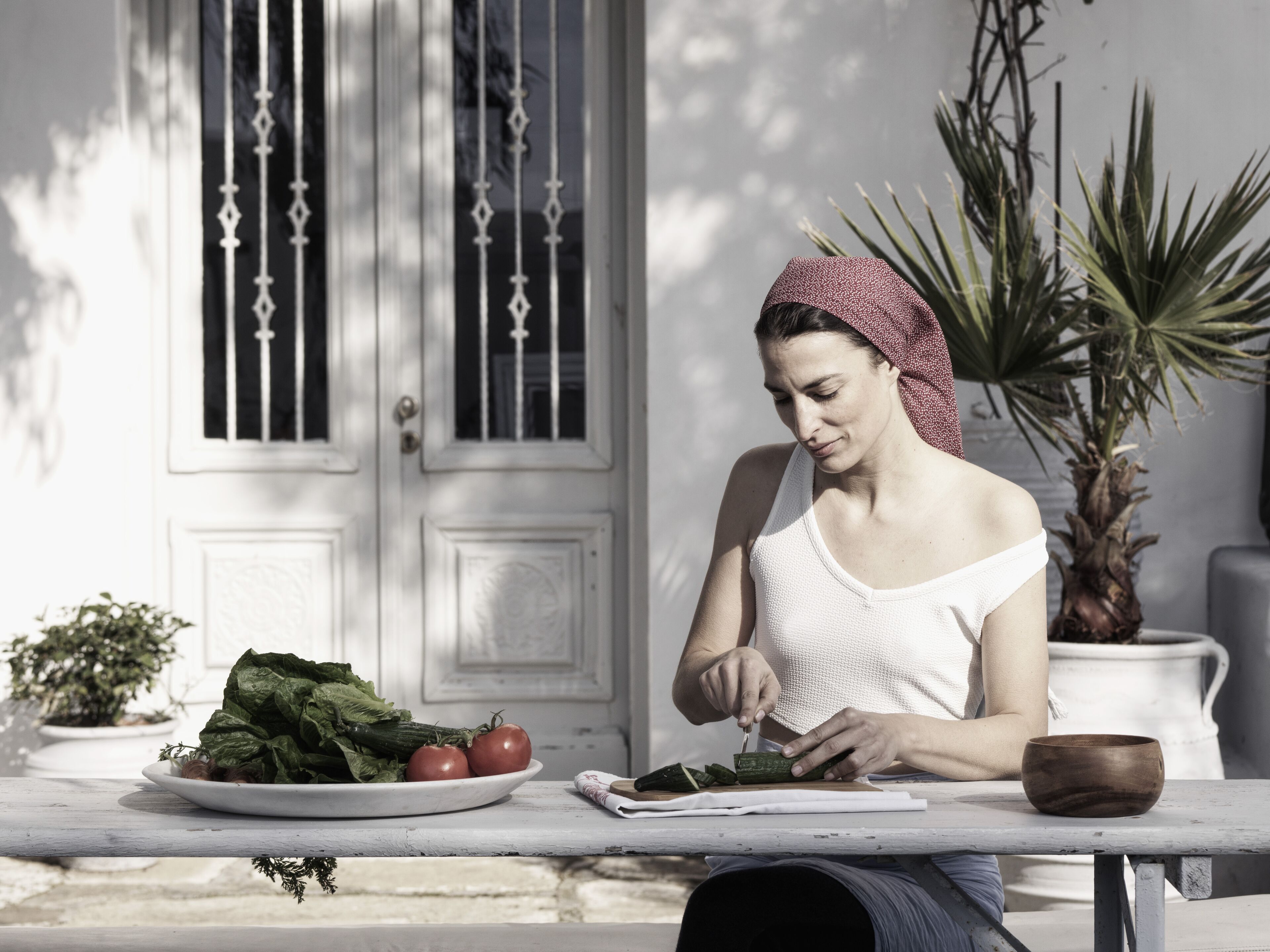 A person preparing food at a table with a plate of vegetables, a bowl, and a book.