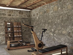 Una habitación con pared de piedra, un banco de madera y una bicicleta estática.