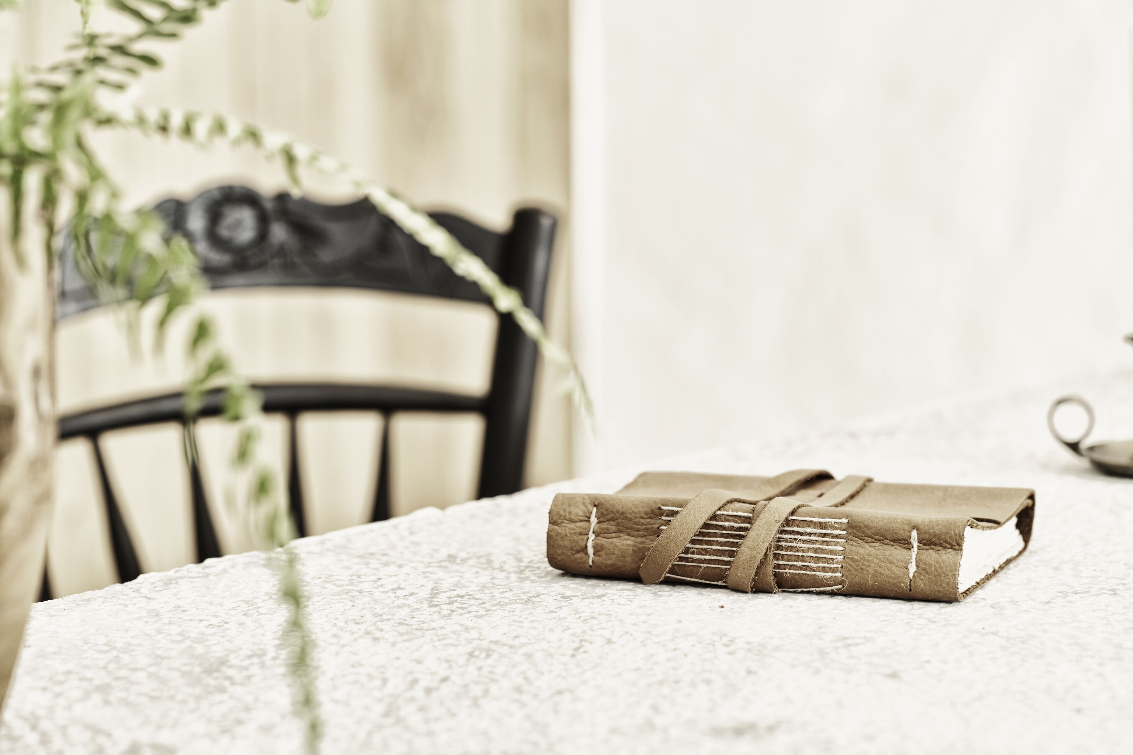 A rolled-up book on a textured table with a chair in the background.