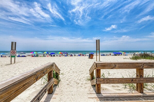 A beach with wooden boardwalks, umbrellas, and a sign prohibiting fireworks.