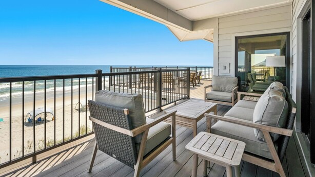 A balcony with wicker furniture, a table, and a view of the beach and ocean. - Penthouse Oceanfront Villa at Inlet Point on Litchfield Beach (Pawleys Island)