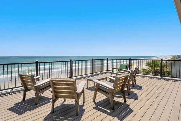 A wooden deck with outdoor furniture overlooking a beach.