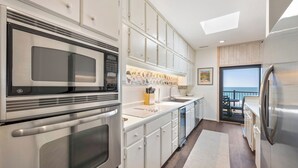 A modern kitchen with stainless steel appliances, white cabinetry, and a view to the outside. - Penthouse Oceanfront Villa at Inlet Point on Litchfield Beach (Pawleys Island)