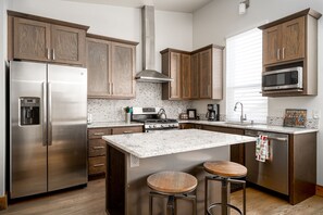 A modern kitchen with wooden cabinets, stainless steel appliances, a central island with stools, and a microwave above the sink.