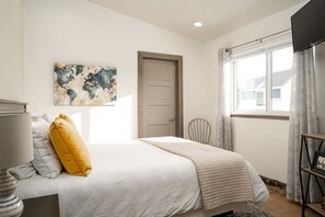 A bedroom with a bed, a map artwork, a door, a window with curtains, and a TV.